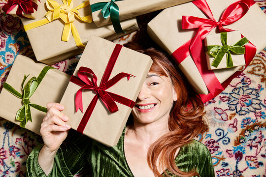 Smiling woman in velvet dress holds a Christmas gift on a rug indoors