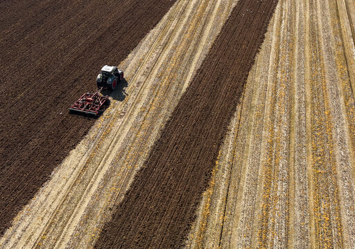 Aerial view of a tractor harrowing farmland in preparation for planting season, showcasing sustainable soil cultivation methods in Sesto Ulteriano, Lombardy, Italy.