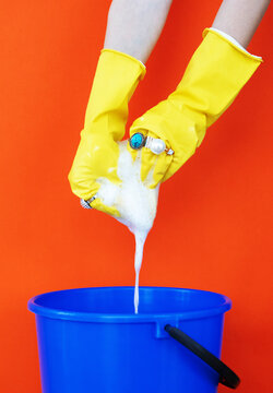 Yellow cleaning gloves with rings squeeze foam into a blue bucket