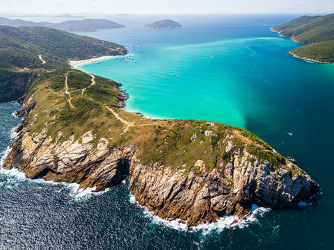 Aerial view of the turquoise waters of Arraial do Cabo, featuring rugged rocky cliffs, a sandy beach, and boats in the bay, Arraial do Cabo, State of Rio de Janeiro, Brazil.