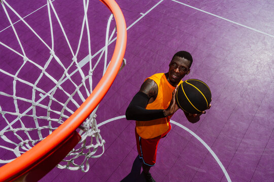 Male basketball player aims ball at hoop on purple outdoor court