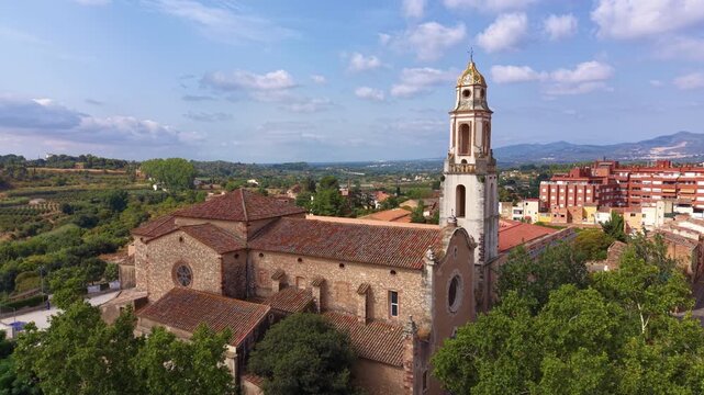 Aerial view of the Baroque bell tower of Esglesia del Carme in Valls, Catalonia, Spain, with glazed ceramic dome, rose window, red-tiled roofline, and mountains in the distance