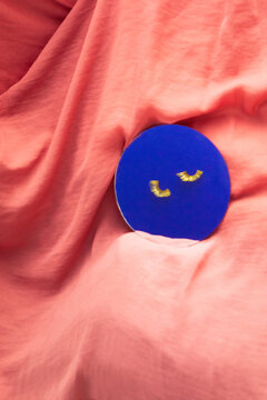 Gold eyelash rests on a blue mirror atop pink fabric