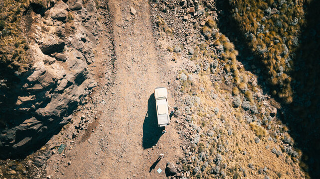 Aerial view of a 4x4 vehicle parked on a rugged dirt road winding through the rocky mountain terrain of Sani Pass, Lesotho, Lesotho.