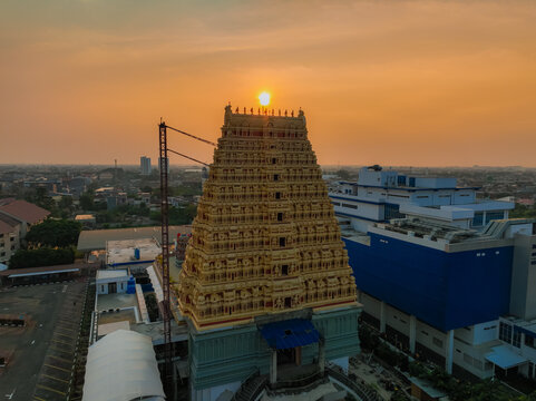 Aerial view of Murugan Temple Jakarta at sunset with golden light illuminating the ornate gopuram tower in Kecamatan Kalideres, Daerah Khusus Ibukota, Indonesia.