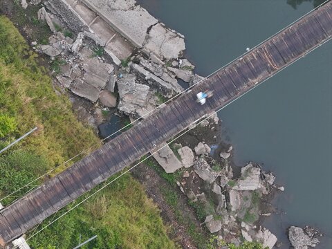 Aerial view of a person crossing a wooden suspension bridge over a river with rocky banks and lush greenery in Yogyakarta, Special Region of Yogyakarta, Indonesia.
