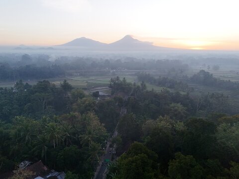Aerial view of the lush landscape near Yogyakarta with volcanoes in the background under a soft sunrise sky, featuring vegetation in Yogyakarta, Special Region of Yogyakarta, Indonesia.