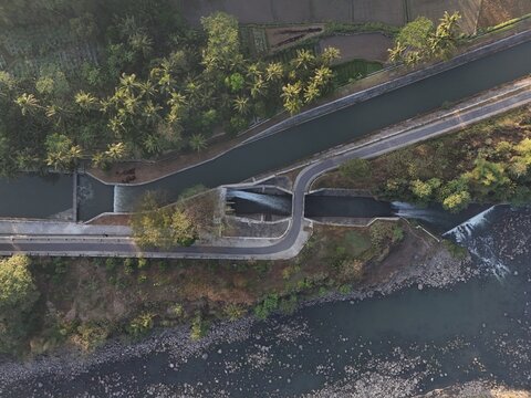 Aerial view of an irrigation canal and dam structure surrounded by lush tropical vegetation and palm trees in Yogyakarta, Special Region of Yogyakarta, Indonesia.