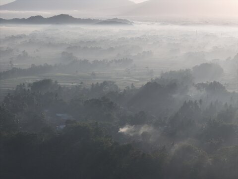 Aerial view of the misty landscape surrounding Yogyakarta with dense vegetation and distant mountains bathed in soft morning light in Yogyakarta, Special Region of Yogyakarta, Indonesia.