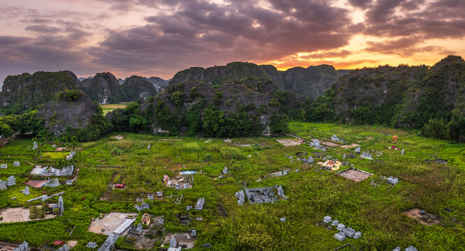 Aerial view of Tam Coc Bich Dong featuring traditional tombs in lush fields surrounded by karst limestone mountains under a sunset sky in Nam Hoa Lu, Ninh Binh, Vietnam.