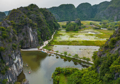Aerial view of the limestone karsts of Tam Coc with winding river channels, lush green rice paddies, and small boats navigating the water in Nam Hoa Lu, Ninh Binh, Vietnam.