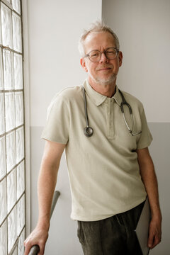 Male doctor with stethoscope stands indoors and looks at camera