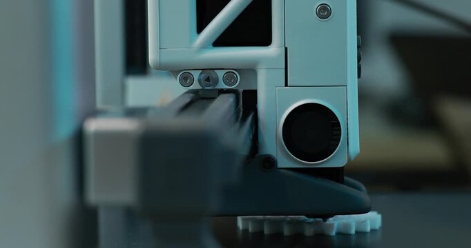 Close-up of a 3d printer nozzle printing a small plastic part with blurred background in a workshop setting