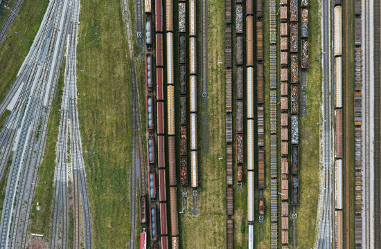 Aerial view of a busy railway yard with numerous freight trains parked on parallel tracks, surrounded by grassy areas and industrial infrastructure in Saalfeld, Thuringia, Germany.