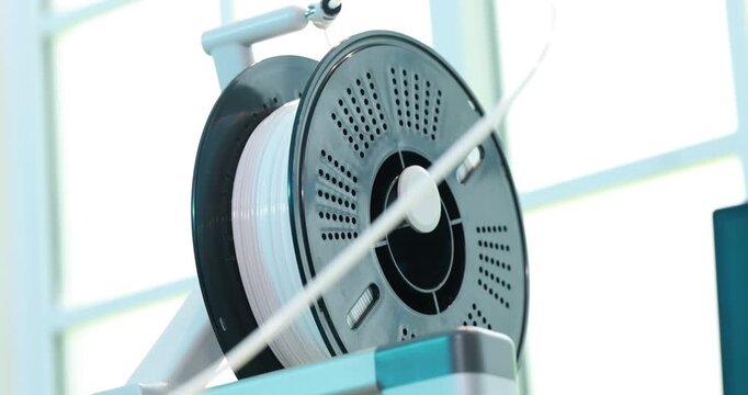 Close-up of a 3d printer filament spool mounted on a holder in a bright workshop, modern making and prototyping equipment.