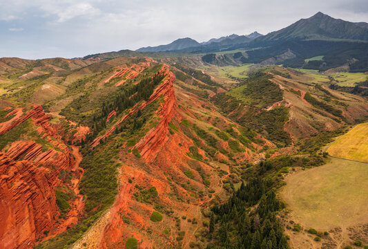 Aerial view of the iconic Seven Bulls Rock red sandstone cliffs surrounded by lush green slopes and coniferous forests in Jeti-Oguz, Issyk-Kul Region, Kyrgyzstan.
