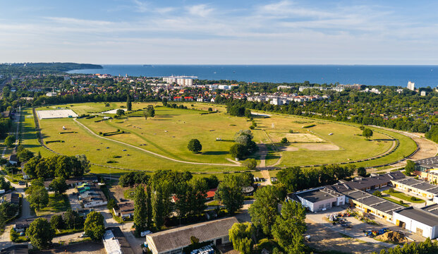 Aerial view of Hipodrom Sopot horse racing track surrounded by green fields and urban landscape with the Baltic Sea in the background in Sopot, Pomeranian Voivodeship, Poland.