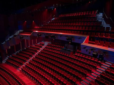 Empty red seats and a technical lighting bridge in a multi level theater auditorium with dramatic red and blue lighting, concert hall.