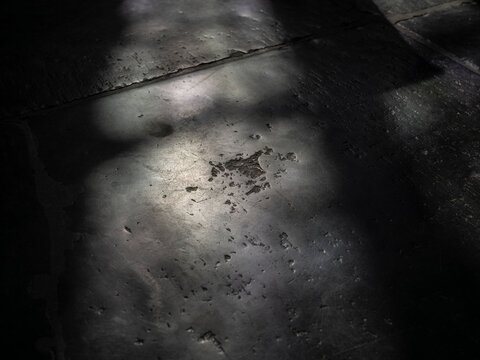 Weathered dark grey stone floor slabs in a shaft of light, scratched and pitted bluestone surface texture for a moody background.