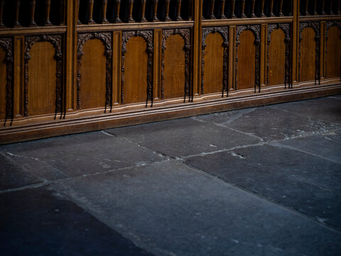 Carved oak choir stalls with arched panels meeting a worn grey stone flag floor in a historic church, heritage woodwork and copy space.