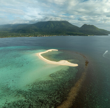 Aerial view of White Island sandbar surrounded by turquoise coral reefs with lush green mountains in the background in Mambajao, Camiguin, Philippines.