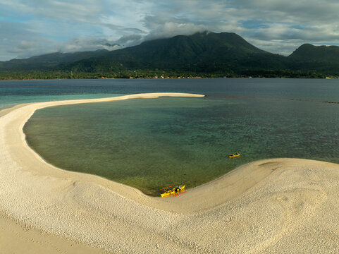 Aerial view of White Island sandbar surrounded by turquoise waters with a traditional outrigger boat moored on the shore and distant mountains in Mambajao, Camiguin, Philippines.