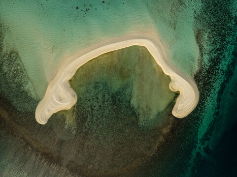 Aerial view of White Island, a crescent-shaped sandbar surrounded by turquoise waters and coral reefs in Mambajao, Camiguin, Philippines.