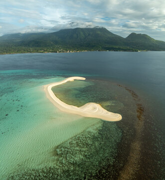 Aerial view of White Island sandbar surrounded by turquoise waters and coral reefs with lush mountains in the background in Mambajao, Camiguin, Philippines.