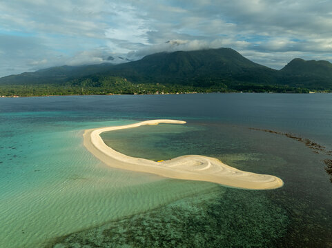 Aerial view of White Island sandbar surrounded by turquoise waters and coral reefs with a mountain backdrop in Mambajao, Camiguin, Philippines.