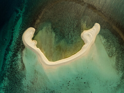 Aerial view of White Island, a crescent-shaped sandbar surrounded by clear turquoise waters and coral reefs in Mambajao, Camiguin, Philippines.