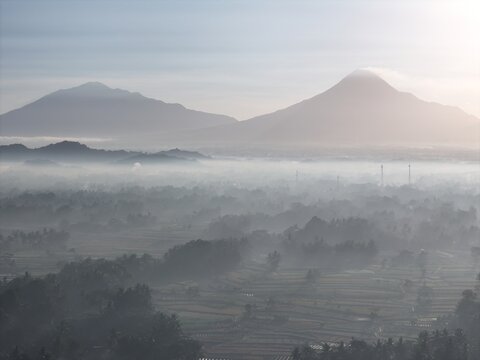 Aerial view of Mount Merapi and Mount Merbabu rising above the misty landscape and terraced fields in Yogyakarta, Special Region of Yogyakarta, Indonesia.