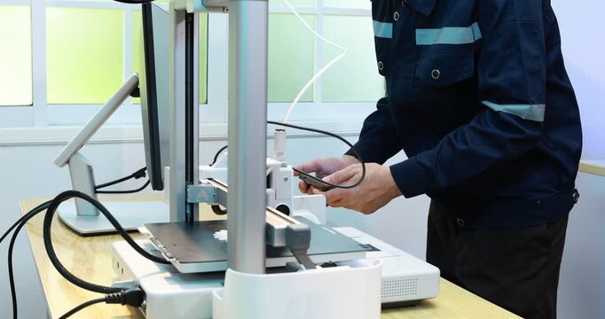 Desktop 3d printer on a workbench in a bright office, with a person standing nearby and cables around the machine.