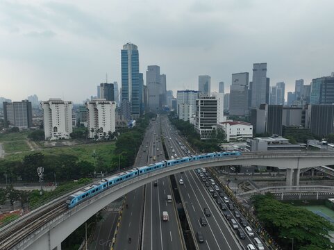 Aerial view of Kuningan district featuring a blue train on elevated tracks above a busy highway surrounded by skyscrapers in Kecamatan Setiabudi, Daerah Khusus Ibukota, Indonesia.