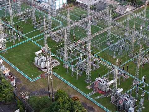 Aerial view of Gardu Induk Sanur electrical substation with high-voltage power lines, metal towers, and transformers in a green compound in Kecamatan Denpasar Selatan, Bali, Indonesia.
