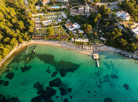 Aerial view of the sandy beach in Thasos, featuring rows of sun loungers, a wooden pier extending into the clear turquoise sea, and surrounding lush pine forests in Thasos, Greece.