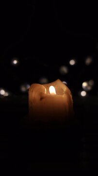 Cinematic close-up of a single burning candle glowing in total darkness, shot with a slow shutter speed. The melted white wax and the warm, steady flame create an intimate atmosphere of silence, hope