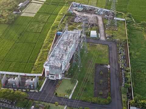 Aerial view of the GIS Tanah Lot electrical substation surrounded by lush green rice paddies and power lines in Kecamatan Kediri, Bali, Indonesia.