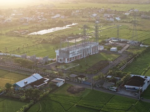 Aerial view of an electrical substation surrounded by lush green rice fields and rural landscape in Kecamatan Kediri, Bali, Indonesia.