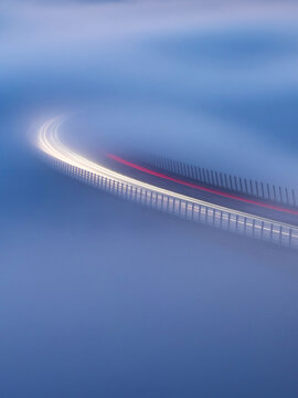 Aerial view of the Crni Kal Viaduct illuminated by vehicle light trails emerging from a thick layer of fog at night in Crni Kal, Koper, Slovenia.