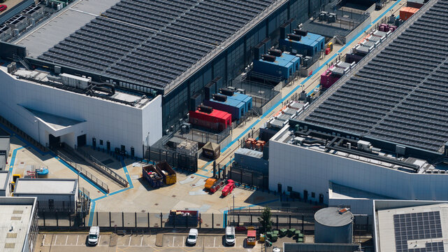 Aerial view of a modern data center facility featuring large rooftops with solar panels, industrial cooling units, and a secure parking area in Hemel Hempstead, England, United Kingdom.