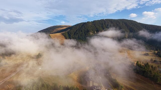 Aerial view of La Molina village and ski slopes partially obscured by thick low fog in the Catalan Pyrenees, Spain, with forested mountain terrain rising above the cloud layer