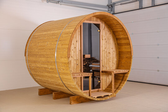 View of a wooden barrel sauna with glass door and exterior benches in Latvia.