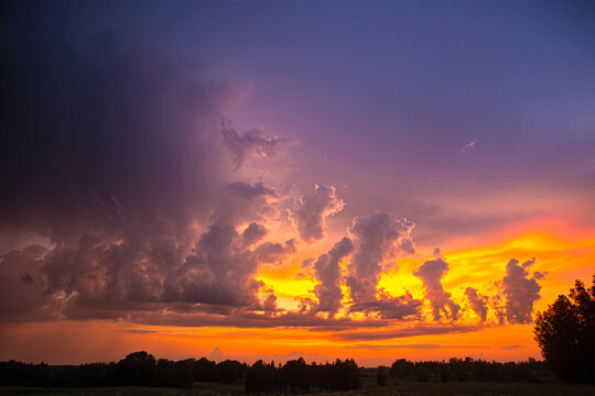 View of a vibrant sunset with dramatic clouds and silhouettes of trees over the landscape in Latvia.