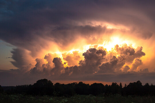 View of dramatic storm clouds illuminated by golden sunset light over the landscape in Latvia.