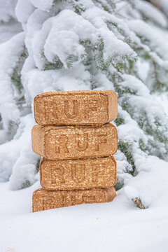 View of a stack of RUF wood fuel briquettes placed in deep snow with a snow-covered pine tree in the background in Latvia.
