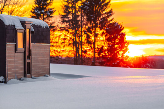 View of a small wooden cabin in a snowy landscape at sunset with pine trees in the background Latvia.