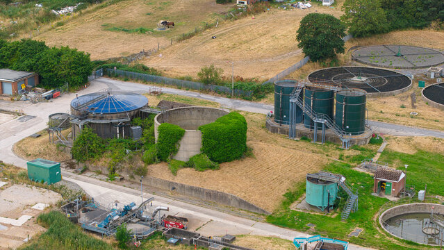 Aerial view of a wastewater treatment plant with circular filtration tanks, green storage silos, and industrial infrastructure in Rainworth, England, United Kingdom.