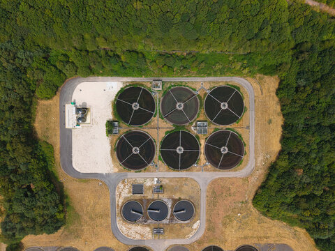 Aerial view of a wastewater treatment plant featuring circular sedimentation tanks and filtration basins surrounded by dense forest in Rainworth, England, United Kingdom.