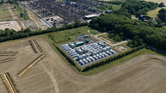 Aerial view of the Pelham Storage Limited battery energy storage facility with white containers in a fenced enclosure near an electrical substation in Bishop's Stortford, England, United Kingdom.