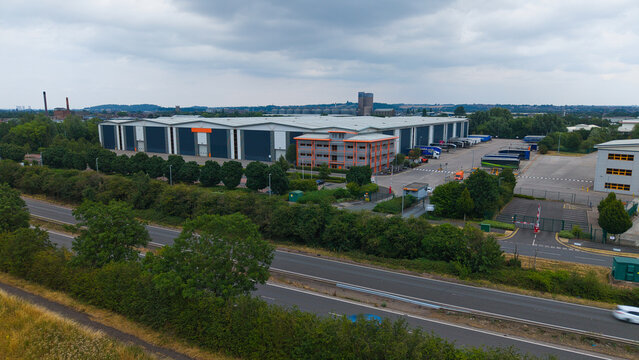 Aerial view of a large industrial warehouse facility with loading bays, office buildings, and surrounding green trees in Burton upon Trent, England, United Kingdom.